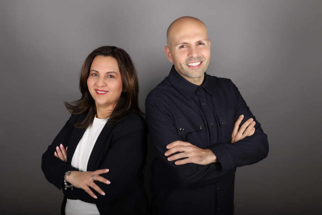 In einem Fotostudio stehen ein lächelnder Mann und eine Frau mit verschränkten Armen.
